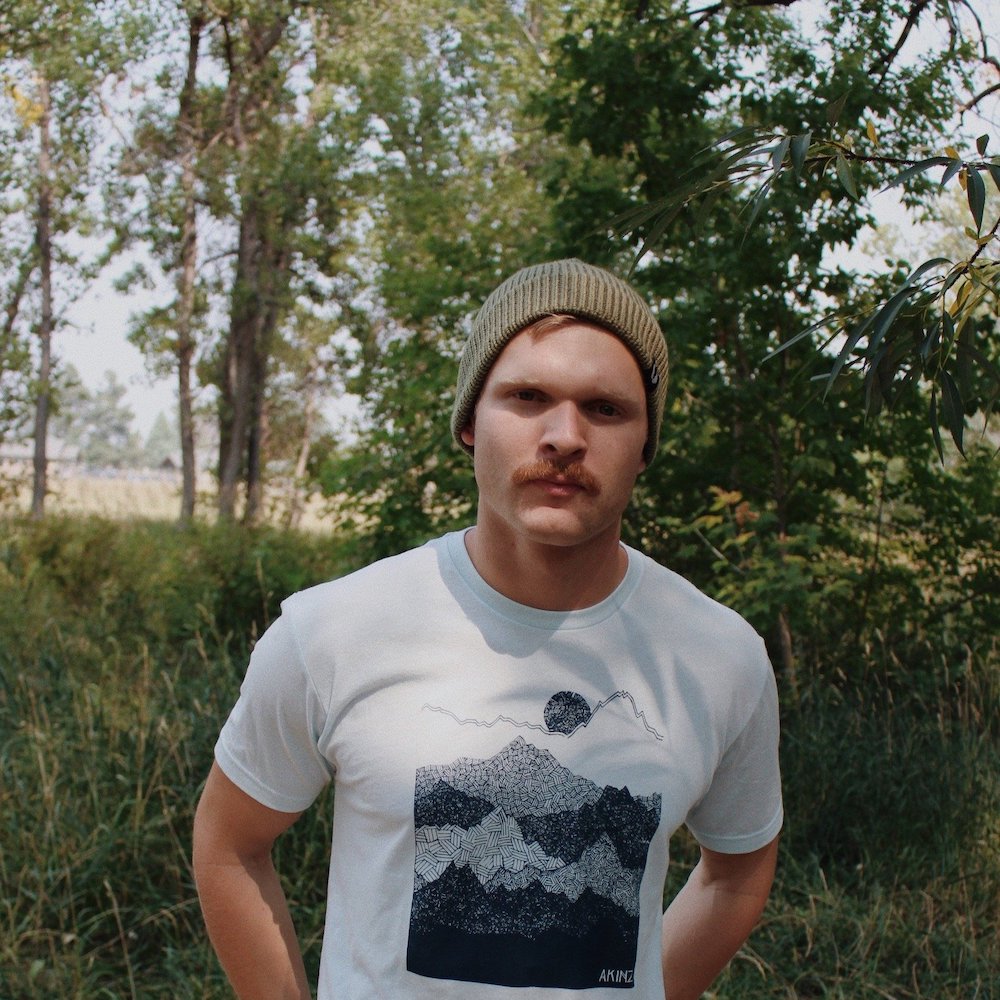 man outside wearing light spruce green ahab knitted beanie and light blue ascend mountain tee